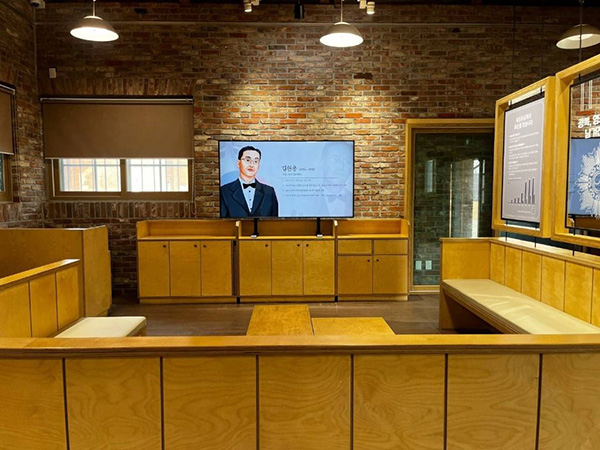 서대문형무소역사관 독립운동가 김원용의 정보를 보여주는 대형 모니터와 나무 벤치가 마련된 실내 전시실 전경