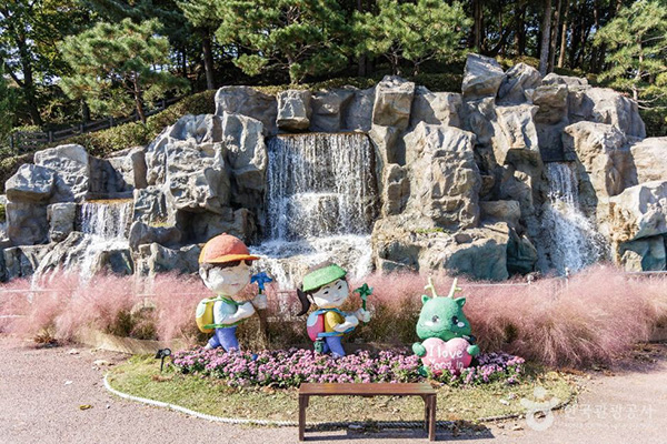 용인농촌테마파크의 인공폭포 앞 분홍색 핑크뮬리와 귀여운 캐릭터 조형물